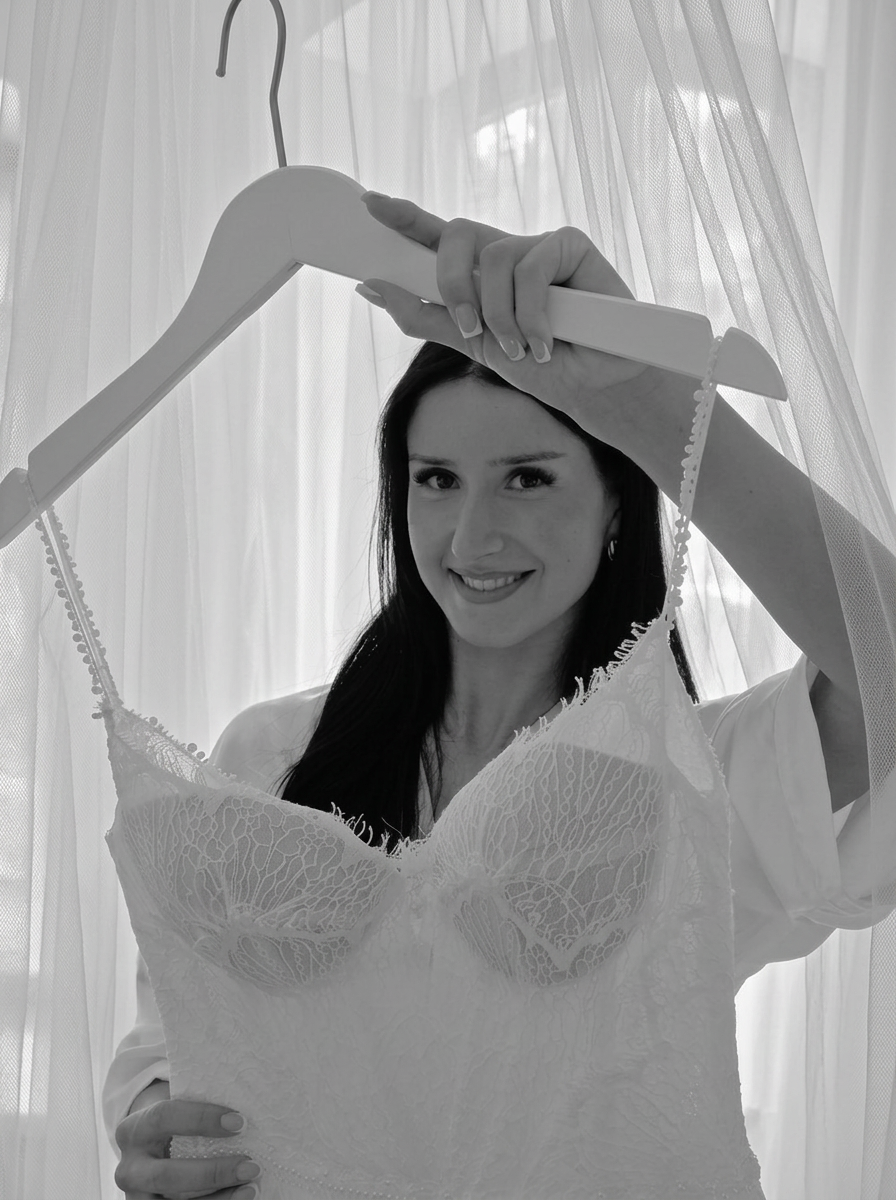 Braut hält ihr Brautkleid mit Spitzencorsage vor sich – Brautmode Nürnberg bei Bella Sposa in Fürth