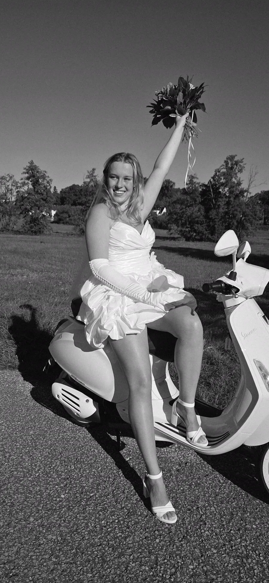 Braut im Minikleid auf der Vespa hebt den Brautstrauß, Schwarzweiß